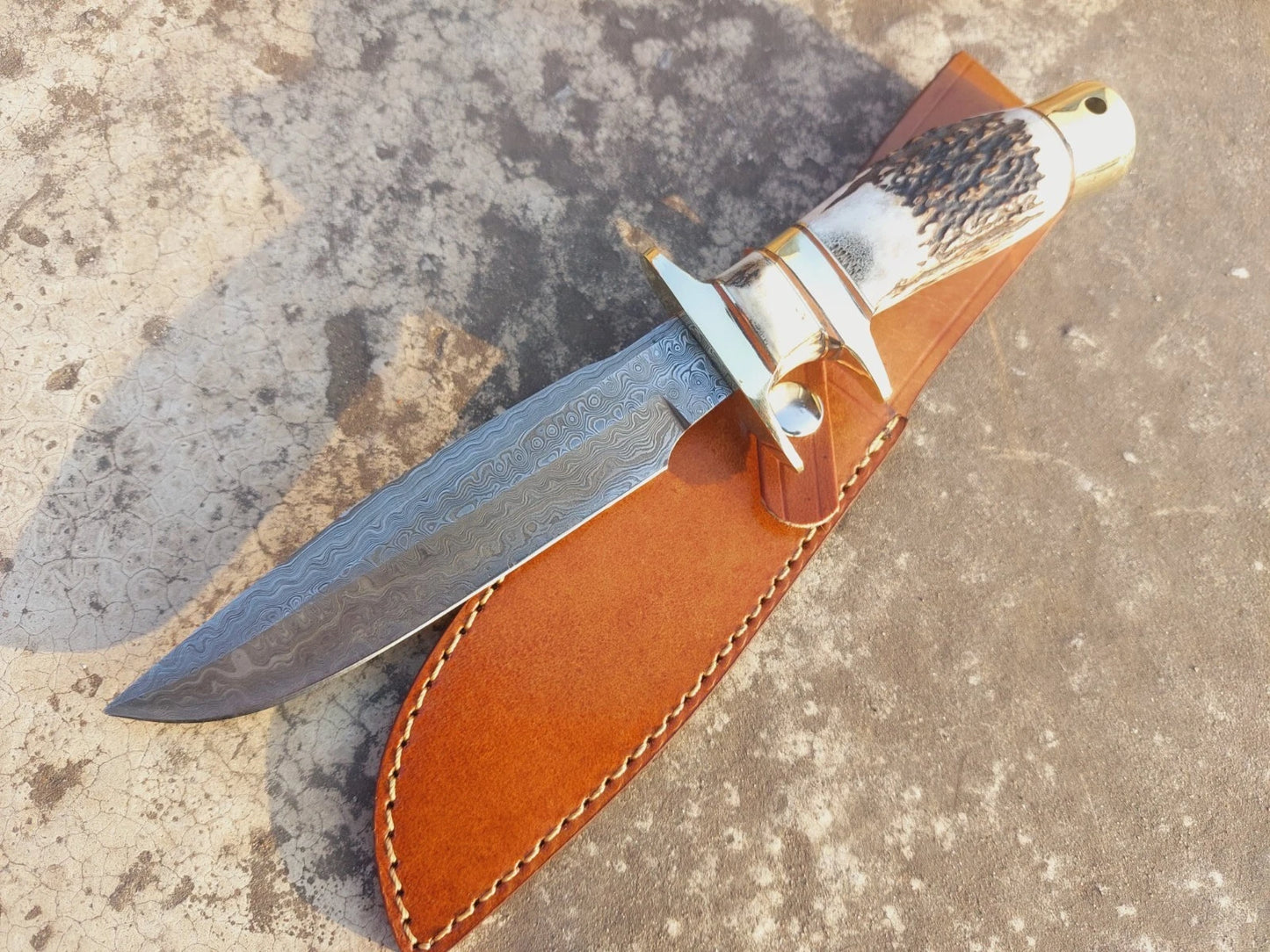 Handmade damascus steel hunting knife, crafted with precision and attention to detail. The natural material handle provides a firm grip, while the guard adds extra protection. This knife combines functionality with artistic blade patterns, making it both practical for outdoor use and appealing as a collectible.