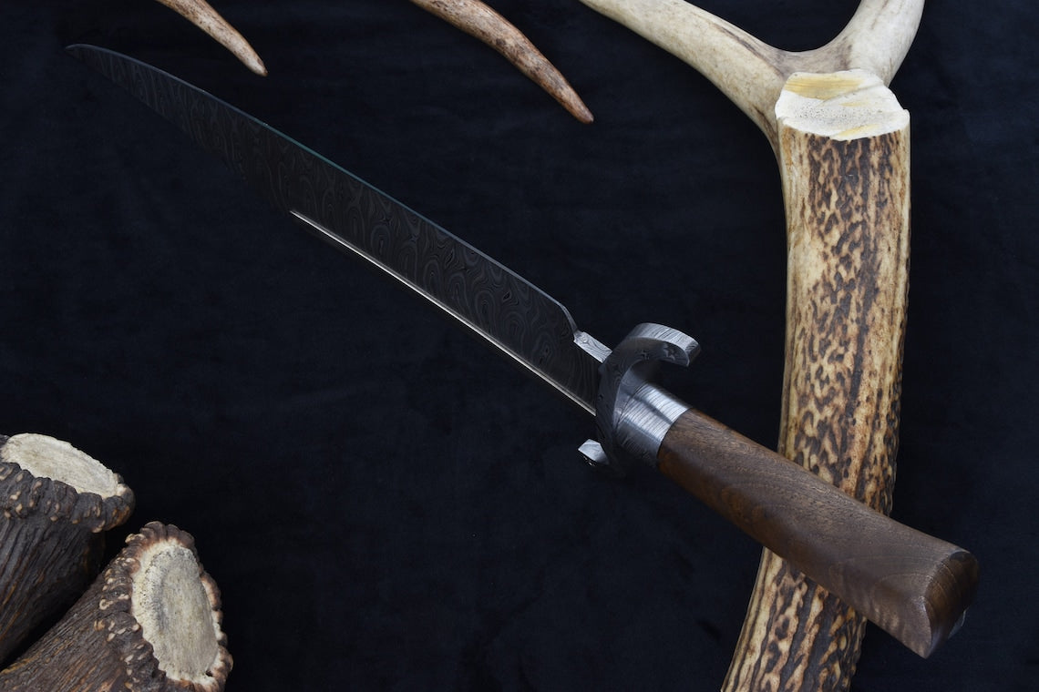 Custom Damascus Texas Bowie knife with walnut handle and layered steel blade patterns, perfect as a collector’s centerpiece or a rugged outdoor companion. Includes a hand-fitted scabbard for protection.