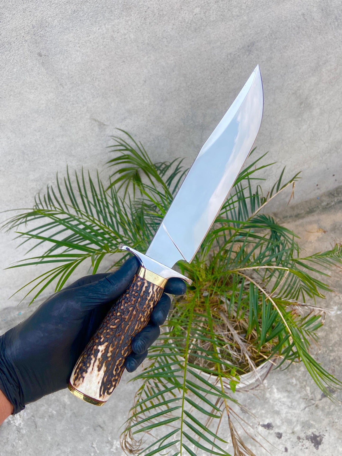 Handmade carbon steel Bowie knife with red-brown leather sheath, crafted for hunters and collectors.