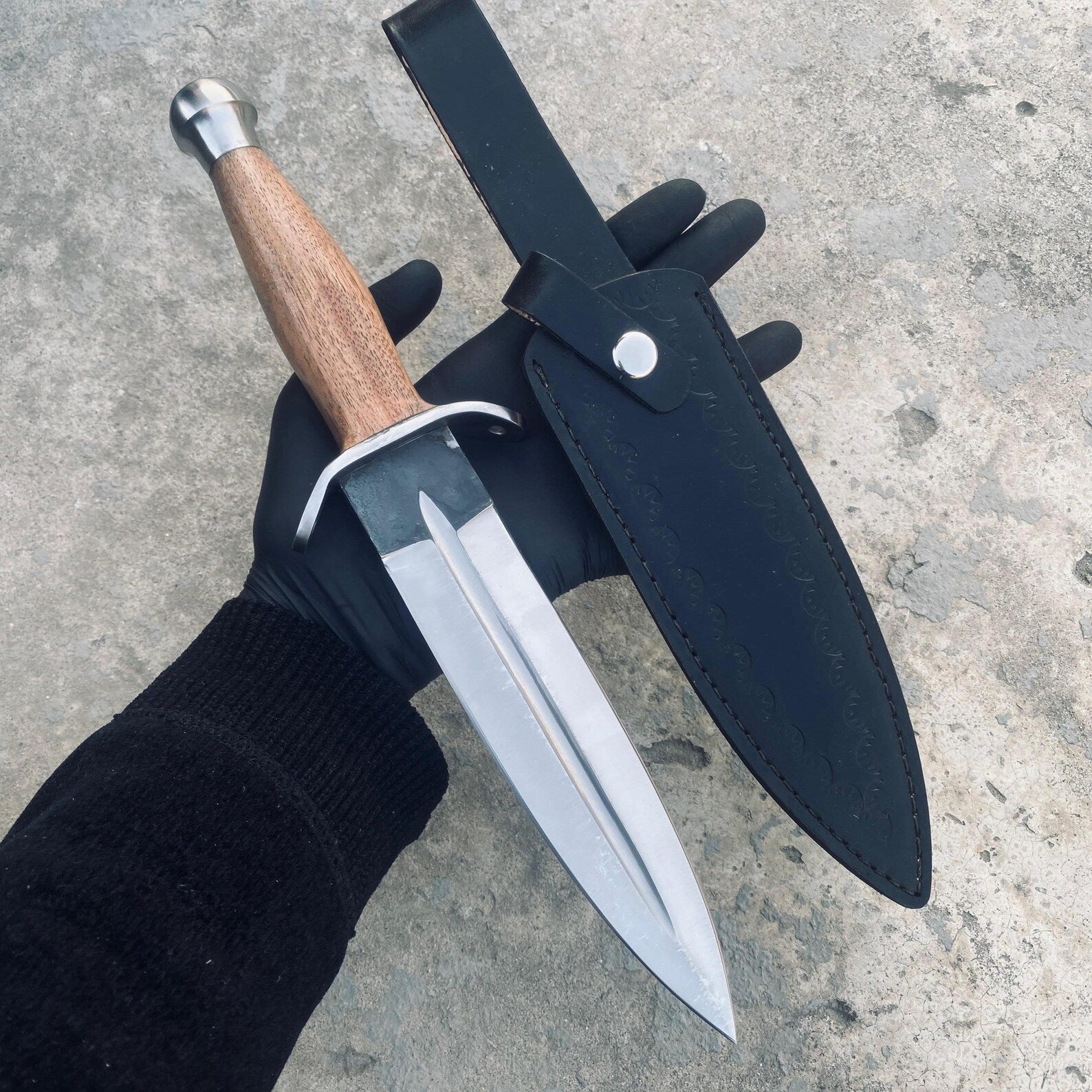 Polished dagger knife resting on rustic wooden background.