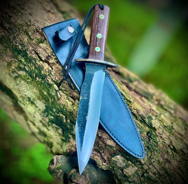 Handmade 5160 carbon steel full tang hunting knife with leather sheath placed on a tree log in outdoor setting.