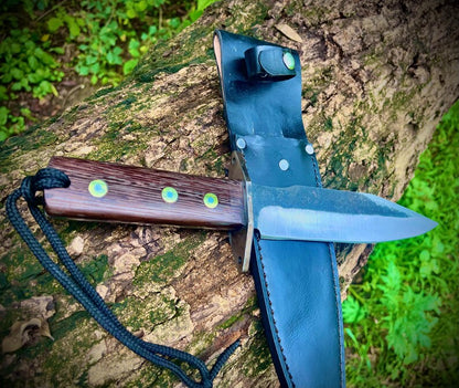 Handmade carbon steel hunting knife placed on black leather sheath showing blade finish and construction.
