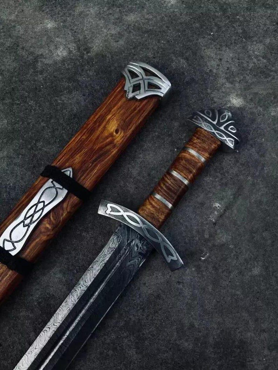 Angled detail of sword guard, fuller, and the carved scabbard throat, demonstrating the matching decorative metalwork and wood grain.