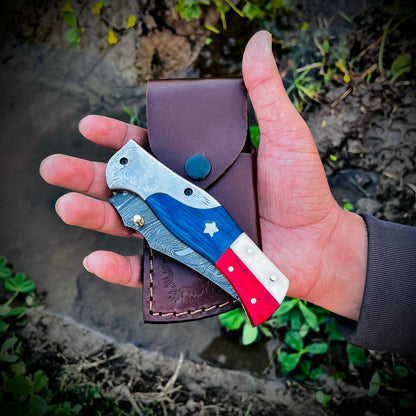 Patriotic Damascus pocket knife with eagle bolster placed on leather pouch highlighting detailed Damascus blade pattern.