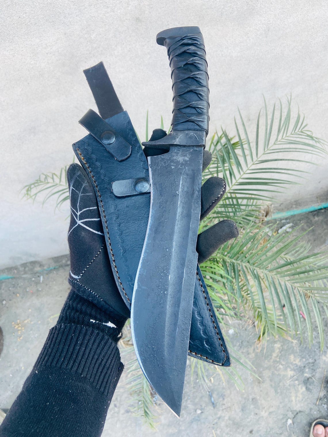 Handmade 5160 spring steel bowie knife with black forged finish and leather-wrapped handle, shown with matching leather sheath.