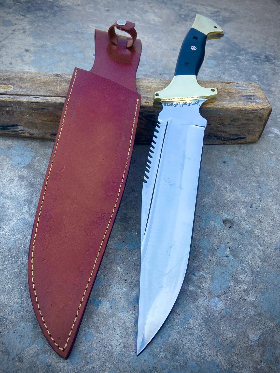 Handmade carbon steel bowie knife with black Micarta and brass handle shown beside premium leather sheath.