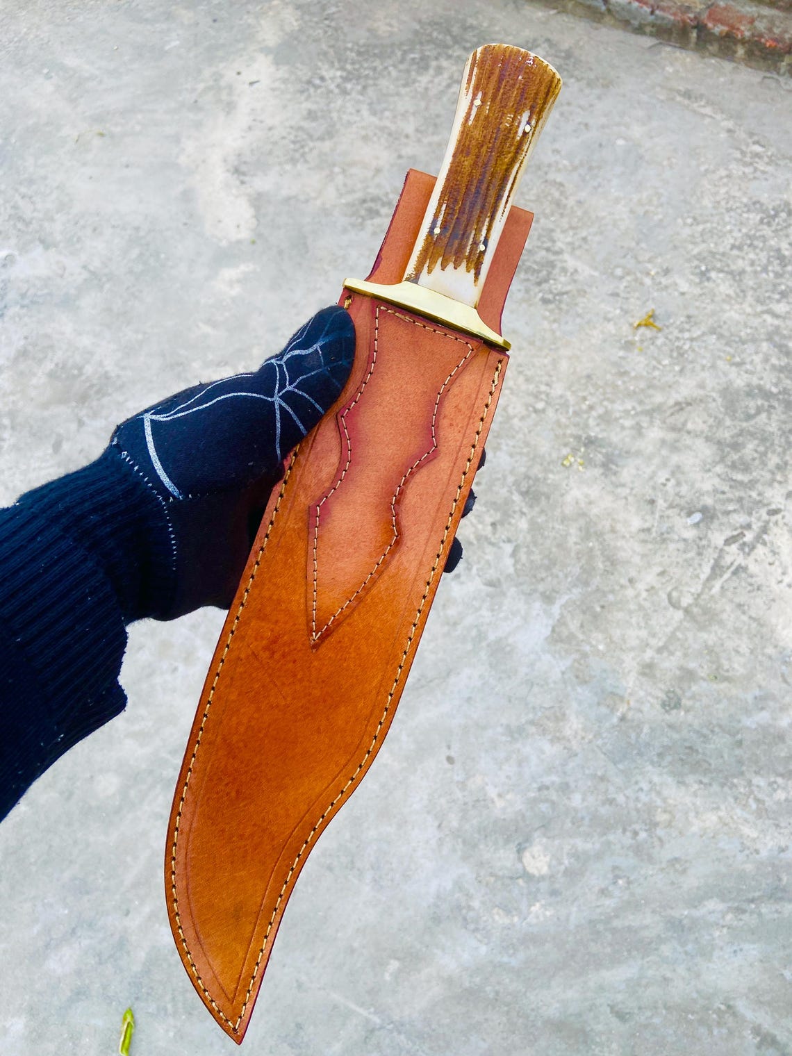 Outdoor shot of D2 steel bowie knife and sheath placed on ground for camping display.