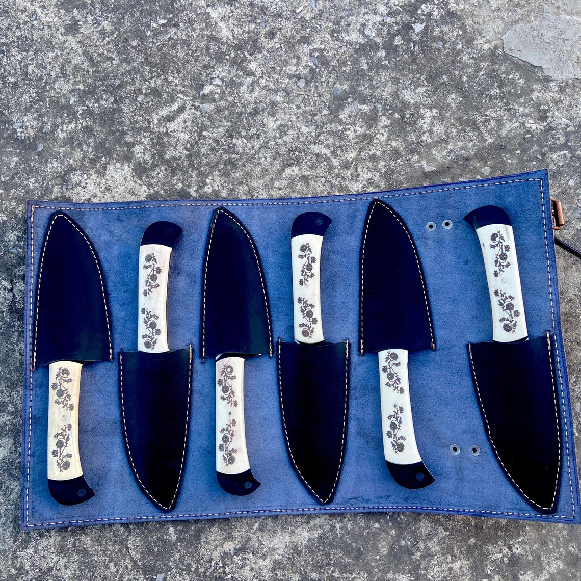 Handmade carbon steel steak knives arranged beside a black leather carrying roll kit.