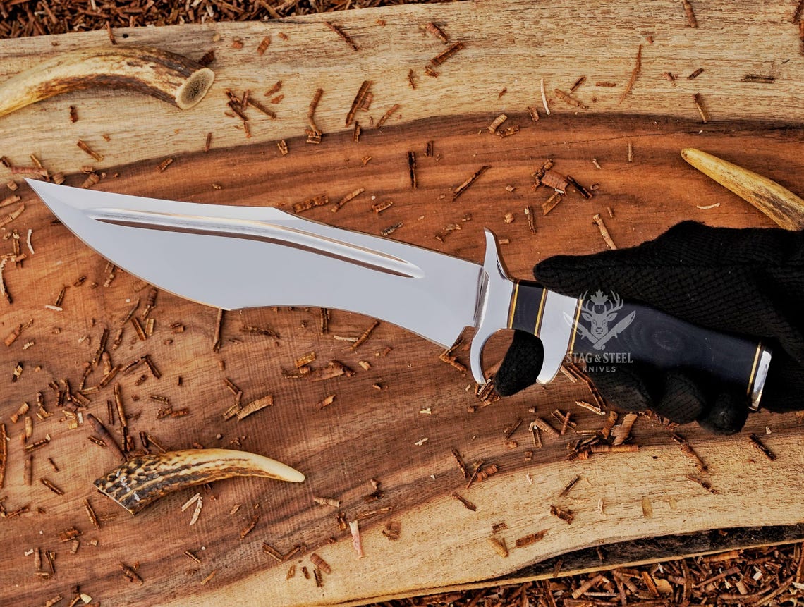 Knife held in hand showing blade profile and blue Micarta handle with brass and steel spacers.
