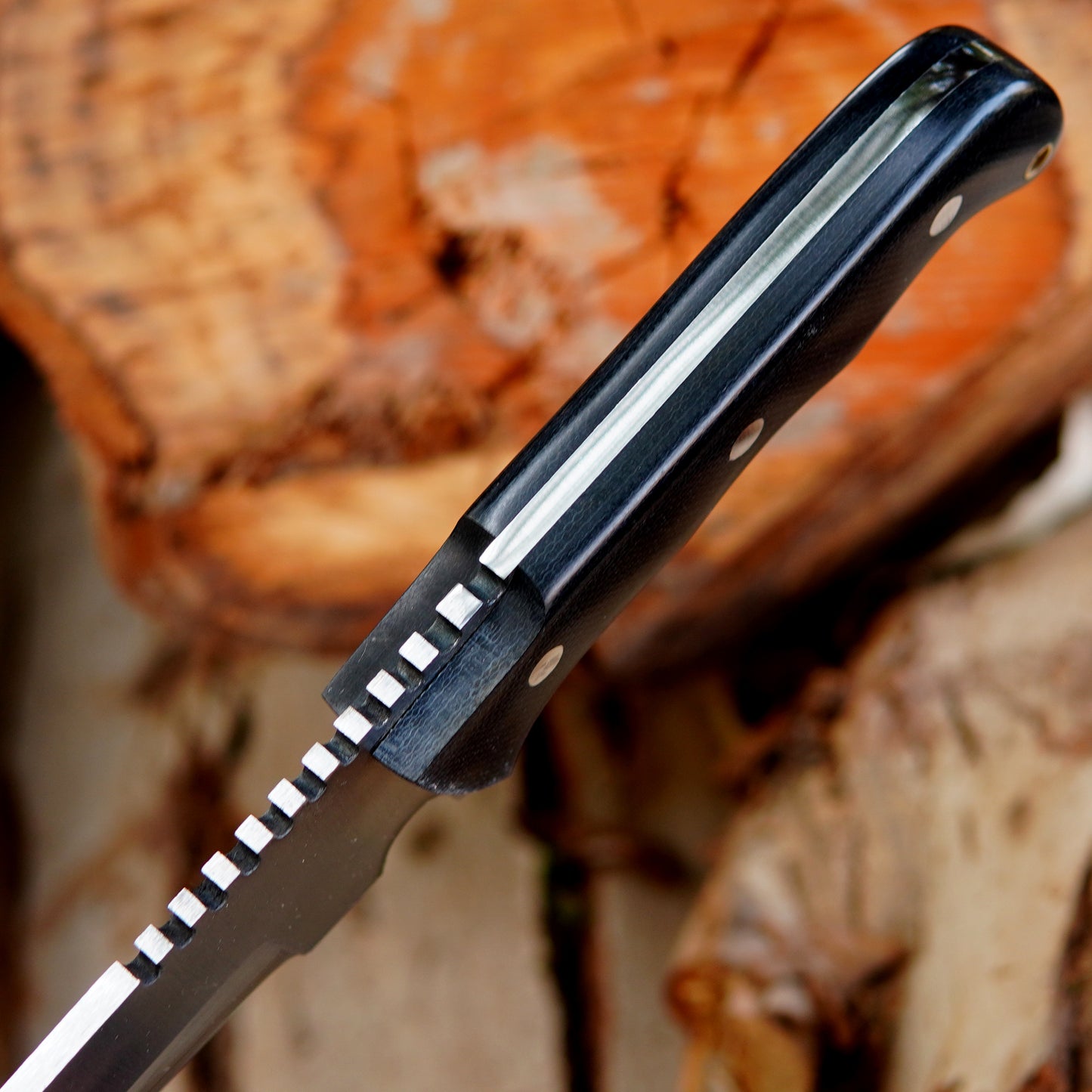 Outdoor display image of handcrafted bowie knife resting on wood surface focusing on blade shape cutting edge alignment and overall handmade finishing suitable for camping hunting and general outdoor activities.