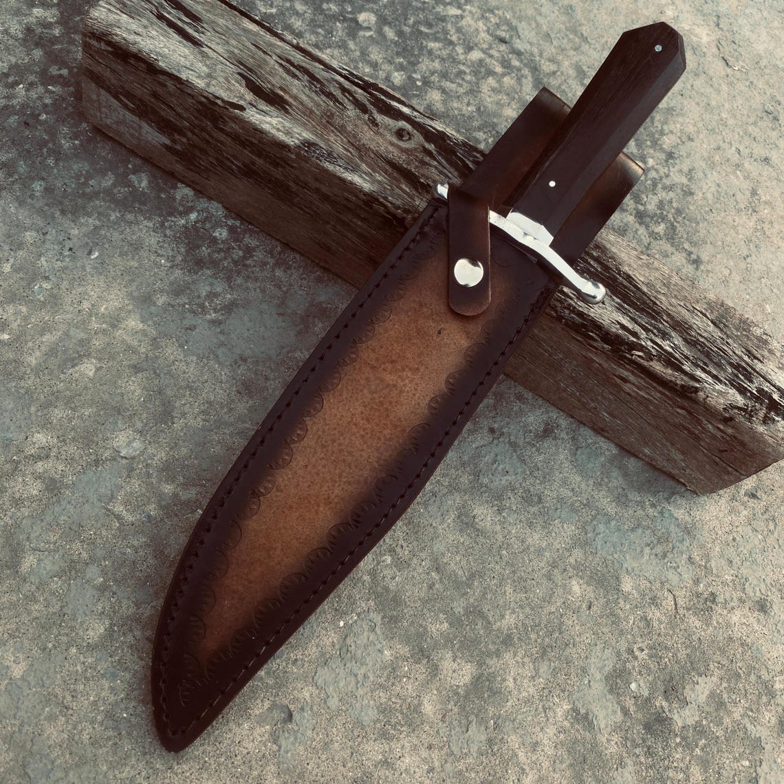 Close-up view of handmade carbon steel Bowie knife held in hand, showing guard and wooden handle.