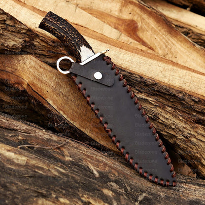 This image captures the Bowie knife resting on a wooden surface with the sharp 1095 carbon steel blade in clear view. The natural stag handle curves upward, showing its rugged texture and organic appearance. The brass guard adds a classic touch to the knife’s design. The background of rough wood emphasizes the handmade and outdoor-ready nature of this unique Bowie knife.