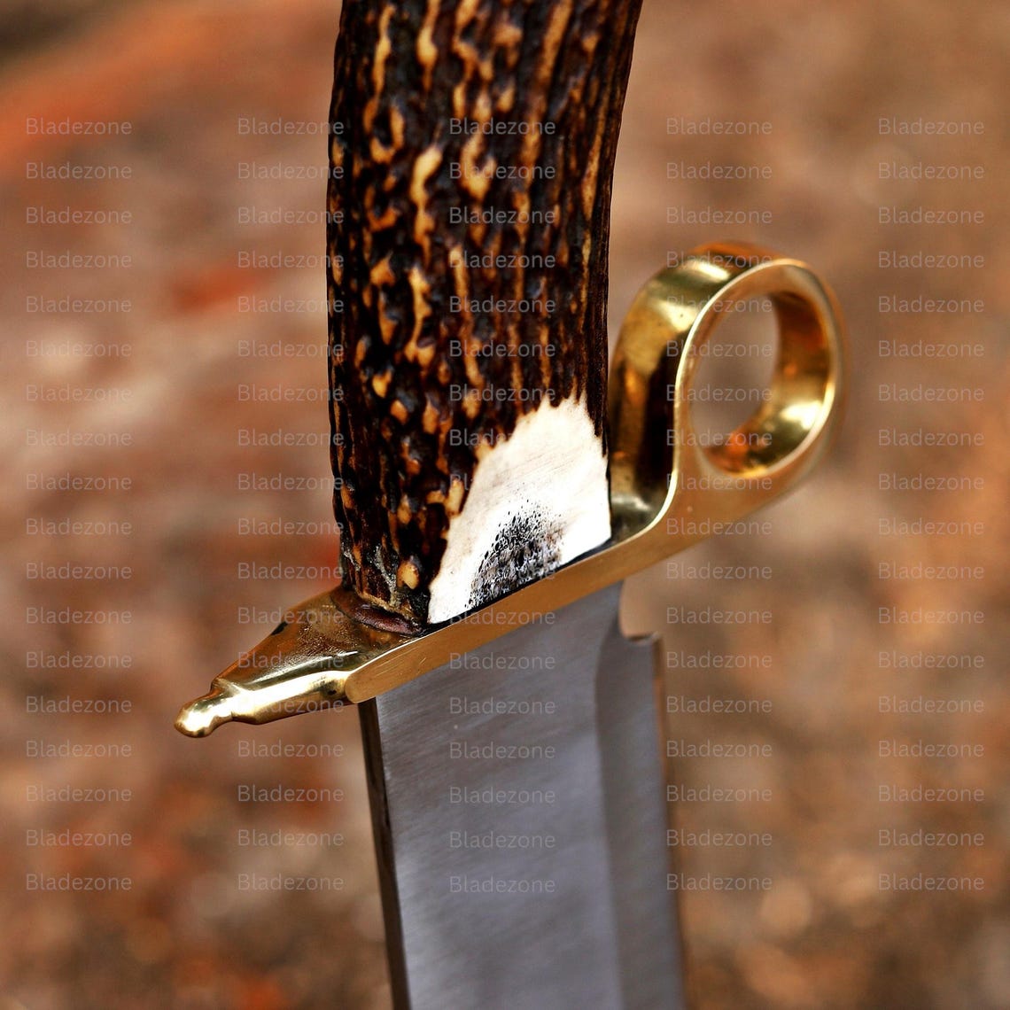 This image features the handmade Bowie knife lying on a textured wooden surface, with the handle positioned toward the camera. The natural stag handle’s cross-section is clearly visible, showing its organic structure. The blade extends outward with a clean finish, while the brass guard offers contrast. The rustic background highlights the knife’s handcrafted quality and rugged outdoor appeal.