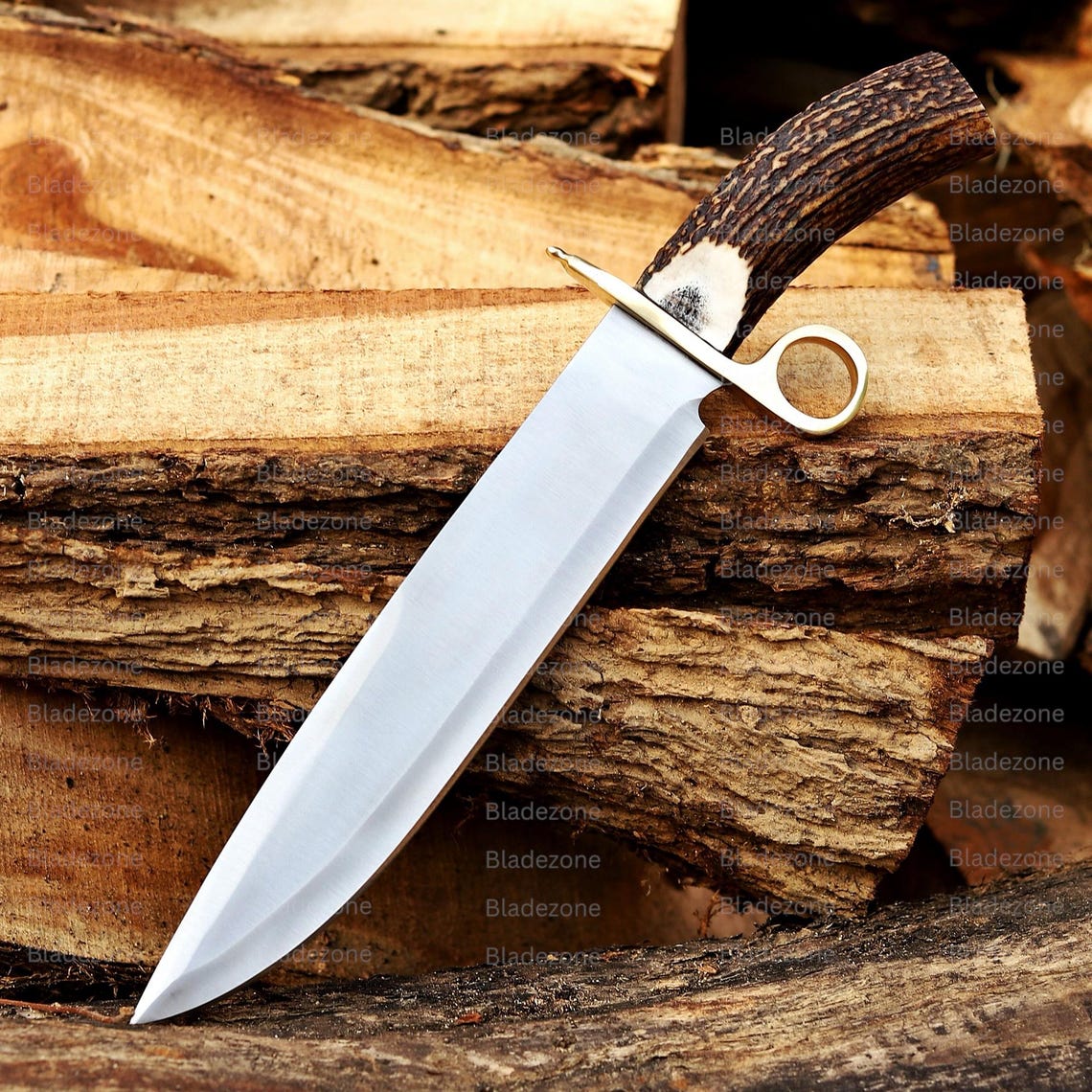 This image showcases a handmade Bowie knife securely placed inside its premium leather sheath, highlighting the natural stag handle’s texture and curved shape. The brown leather sheath features detailed lacing along the border, giving it a rugged look. The knife is placed on stacked wood, emphasizing its outdoor purpose, craftsmanship, and traditional materials used in its construction.