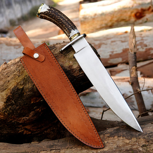 Handmade bowie style knife crafted from 5160 spring steel with a polished blade and premium leather sheath displayed on natural wood.