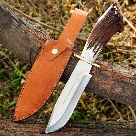 Handmade bowie style knife with polished carbon steel blade and leather sheath displayed on wood.