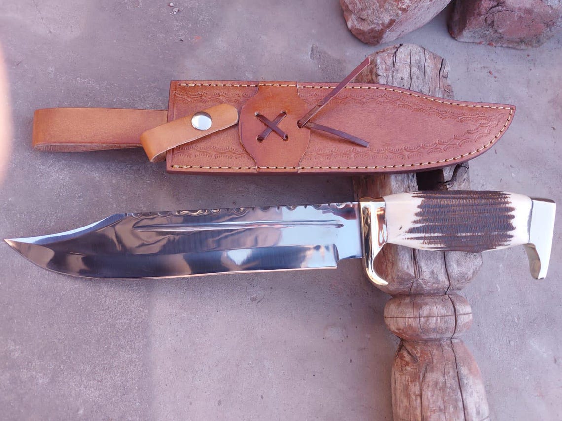 Close-up of handmade Bowie knife showing brass guard and natural stag handle texture.