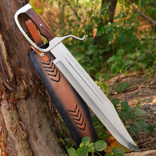 Handmade fixed blade bowie knife placed on natural outdoor wood surface showing sharp high carbon steel blade and smooth grey wood handle with comfortable ergonomic grip designed for camping, hunting, and survival use. The leather sheath is included for safe storage and easy belt carry, making this knife ideal for outdoor adventures and everyday tasks.