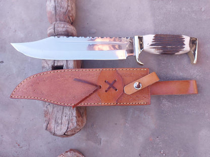Full-length view of handmade Bowie knife beside hand-stitched leather sheath on wooden stand.
