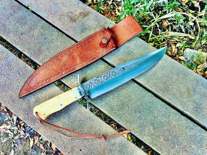 Handmade engraved bowie knife with polished guard and custom leather sheath showing fine stitching.