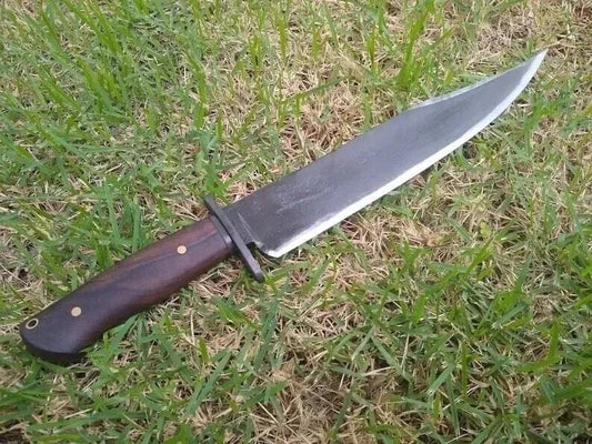 Handmade carbon steel bowie knife with rosewood handle placed on grass