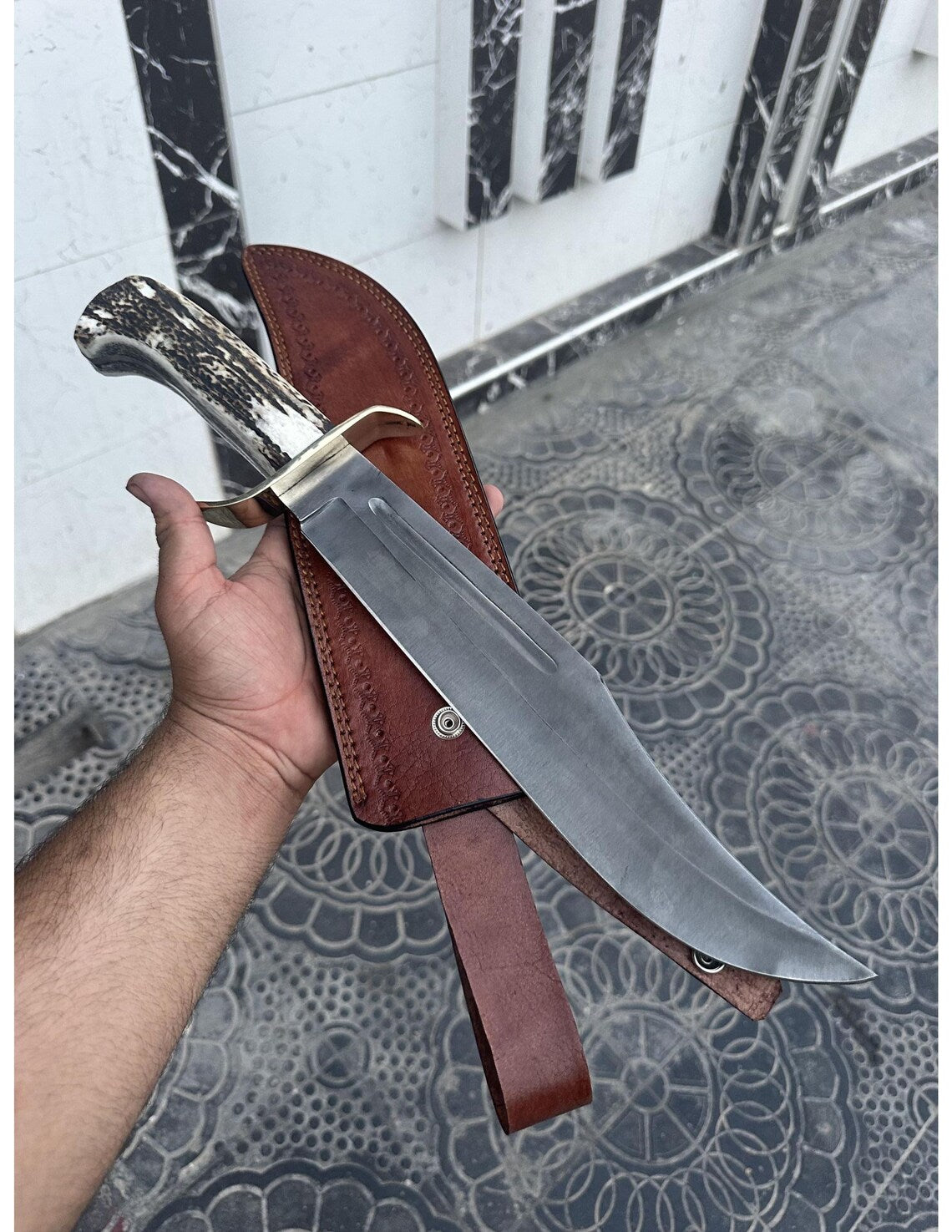 Close-up of handmade Bowie knife showing stag handle and brass guard detailing.