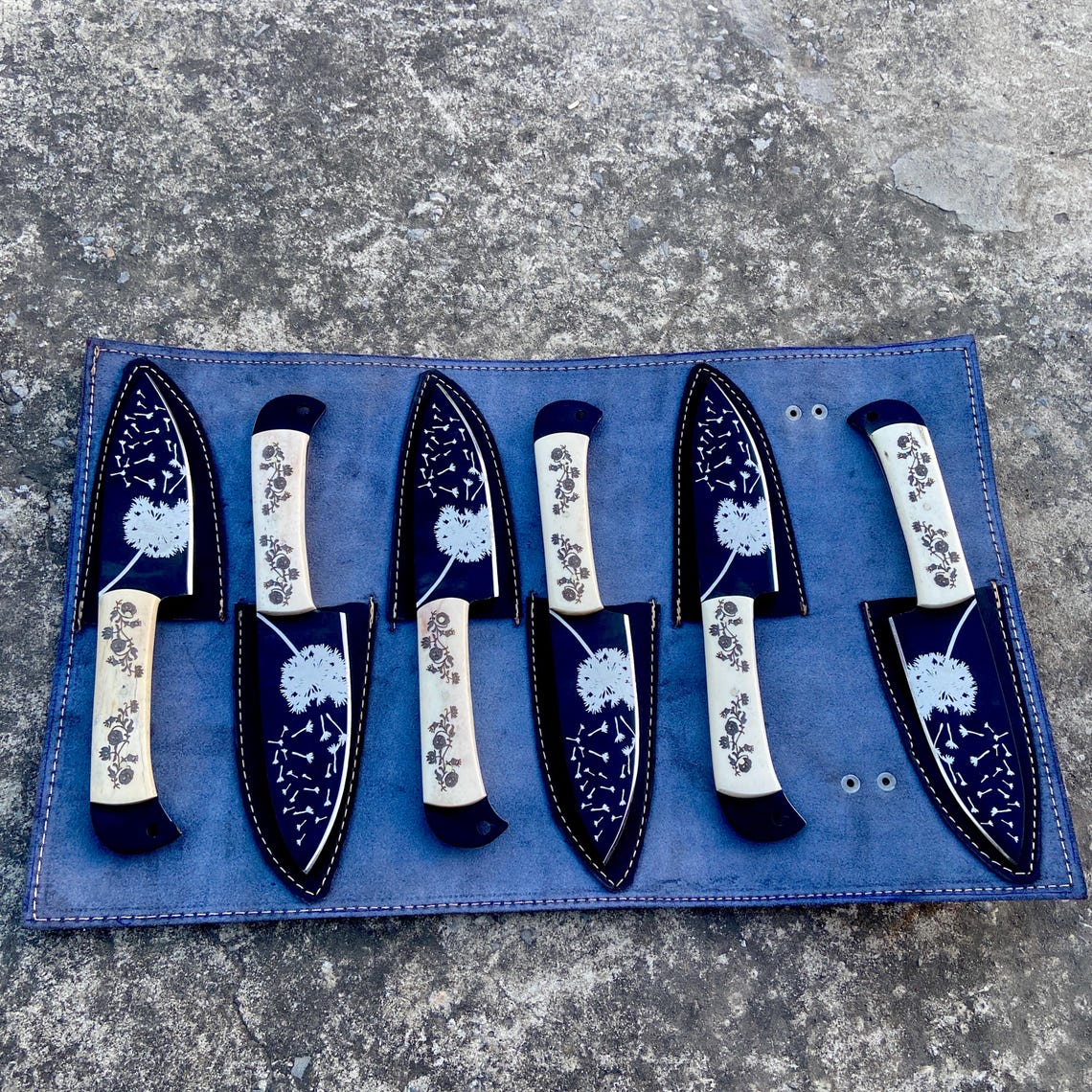 Floral engraved white handle knives with black coated blades displayed outdoors.