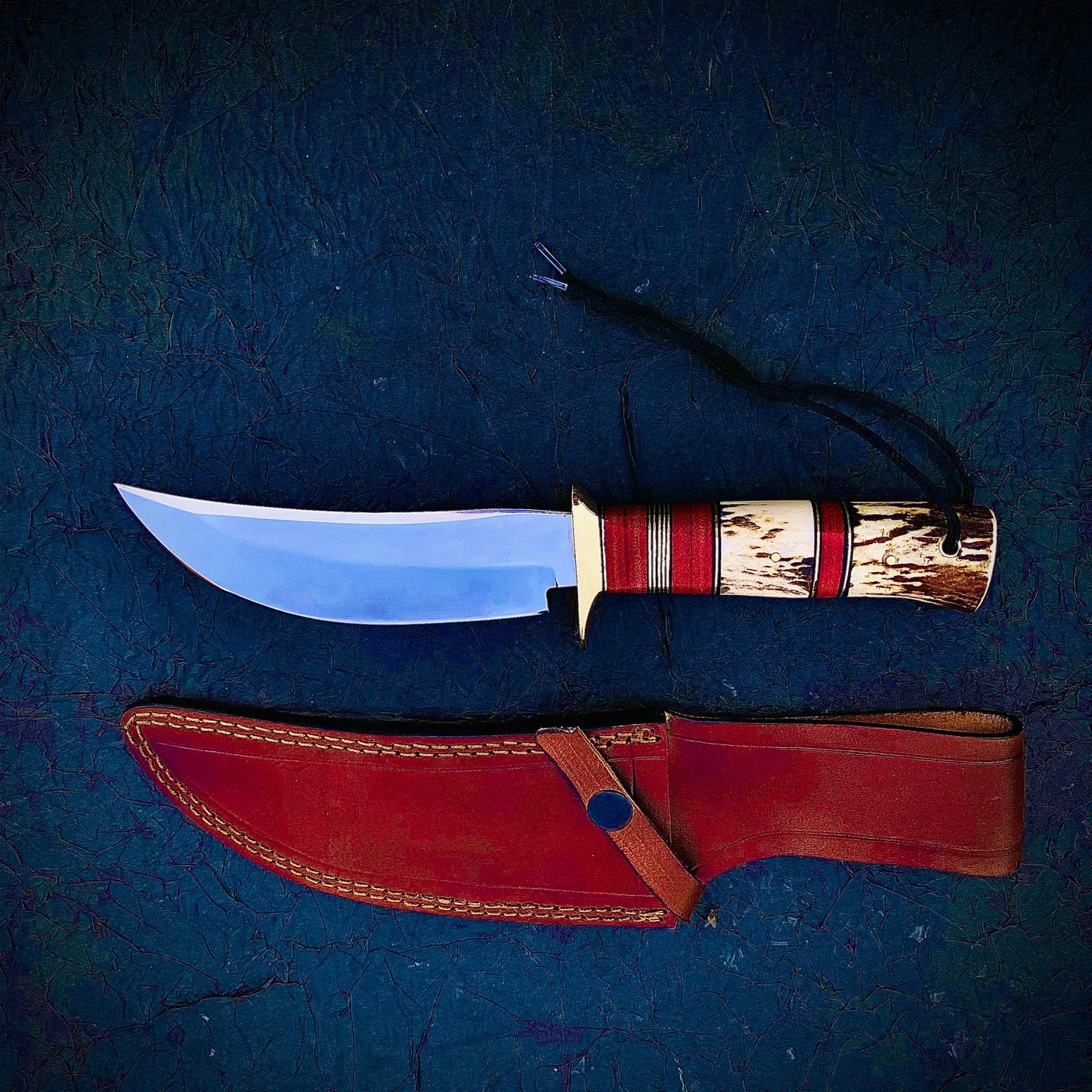 Custom hunting knife crafted from carbon steel with stag antler handle and red micarta accents. Comes with a hand-stitched sheath for safe storage, built for outdoor use and collecting.