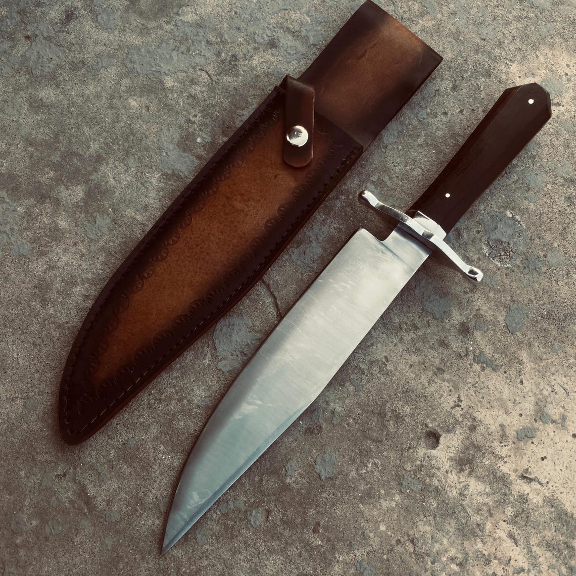 Back view of full-grain leather sheath stitched for Bowie knife, placed on wooden log.