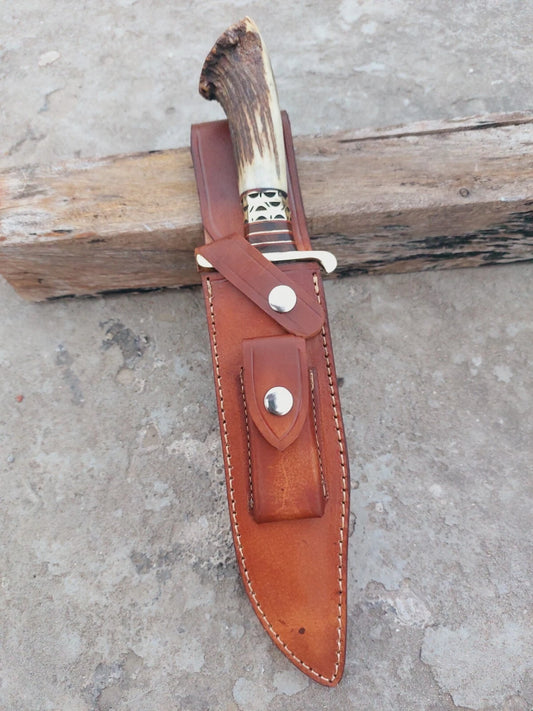 Custom Damascus steel bowie knife with stag handle and crown pommel, featuring brass spacers for balance and detail. The hand-forged blade carries intricate Damascus layers. Supplied with a stitched leather sheath, suitable for hunting, camping, and display collections.