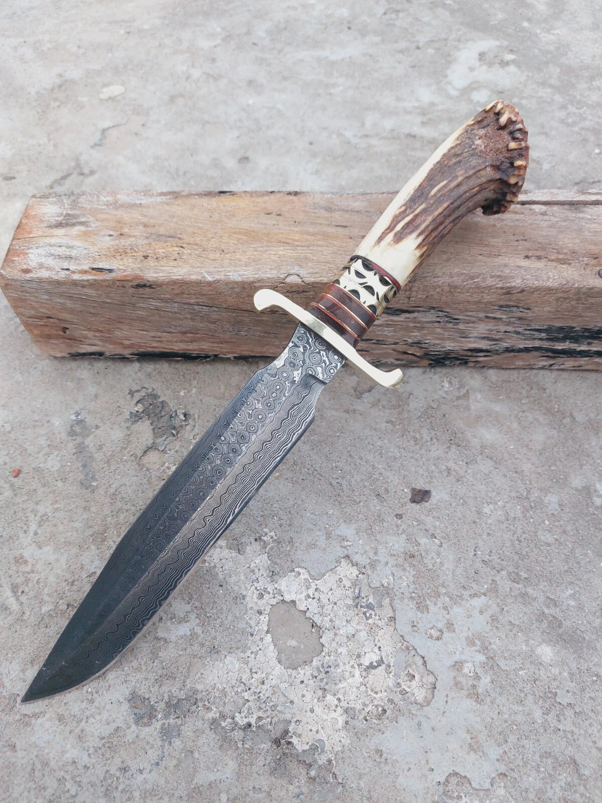 Collector’s Damascus steel bowie knife with a crown stag handle, highlighted by brass spacers and hand-forged blade patterns. The knife is functional for hunting yet elegant for display. Includes a hand-stitched leather sheath.
