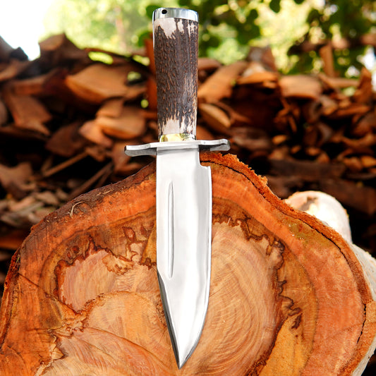 Handmade bowie style knife with polished steel blade, natural material handle, and black leather sheath displayed on wood.