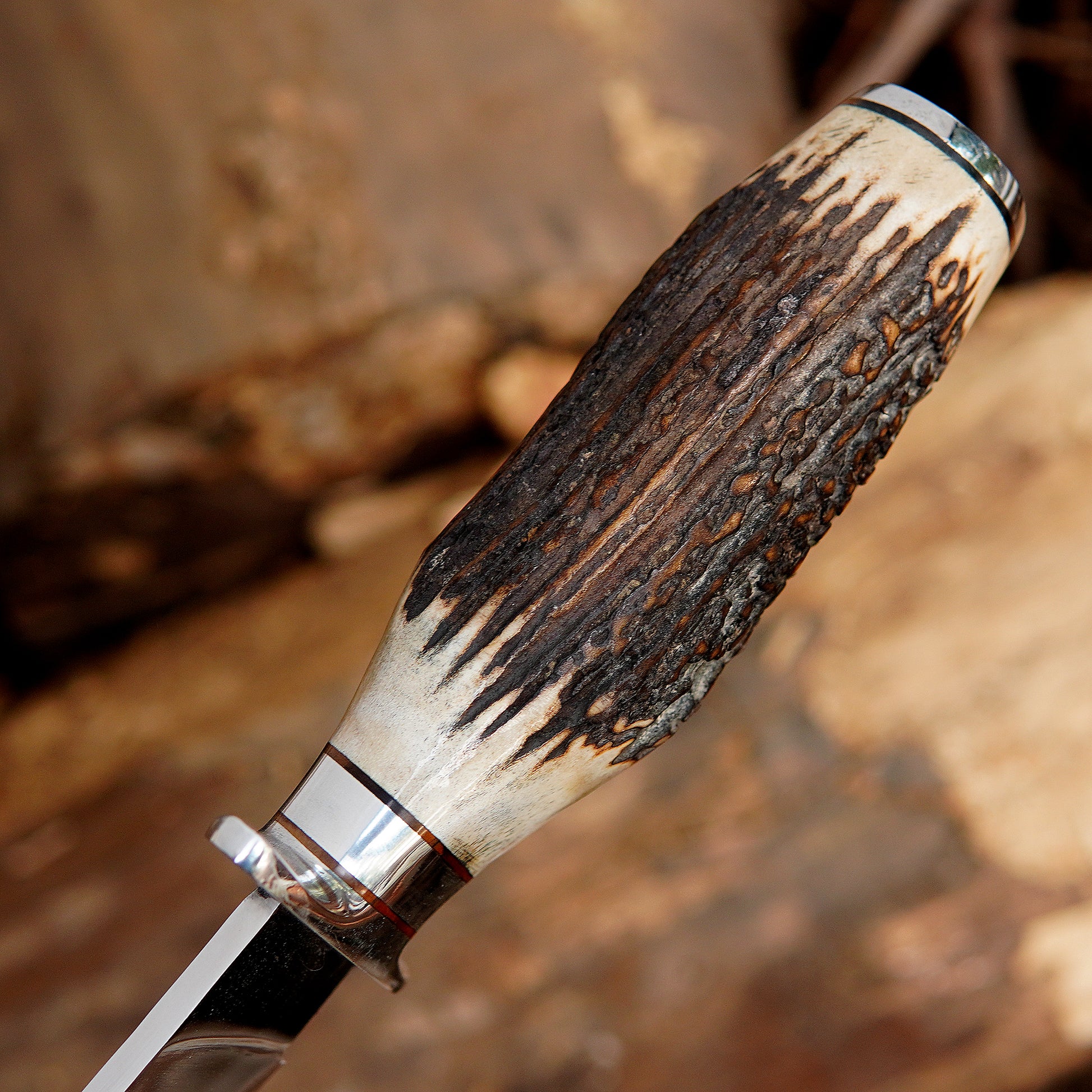 Outdoor survival bowie knife displayed with leather sheath on wooden logs creating a rugged camping atmosphere. The image communicates durability and functionality while appealing to customers looking for outdoor gear, survival tools, or unique handmade knife collections.