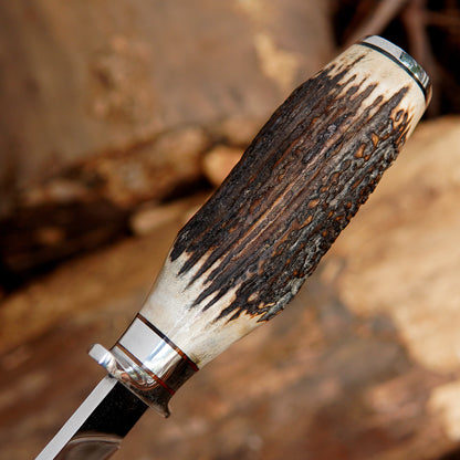 Outdoor survival bowie knife displayed with leather sheath on wooden logs creating a rugged camping atmosphere. The image communicates durability and functionality while appealing to customers looking for outdoor gear, survival tools, or unique handmade knife collections.