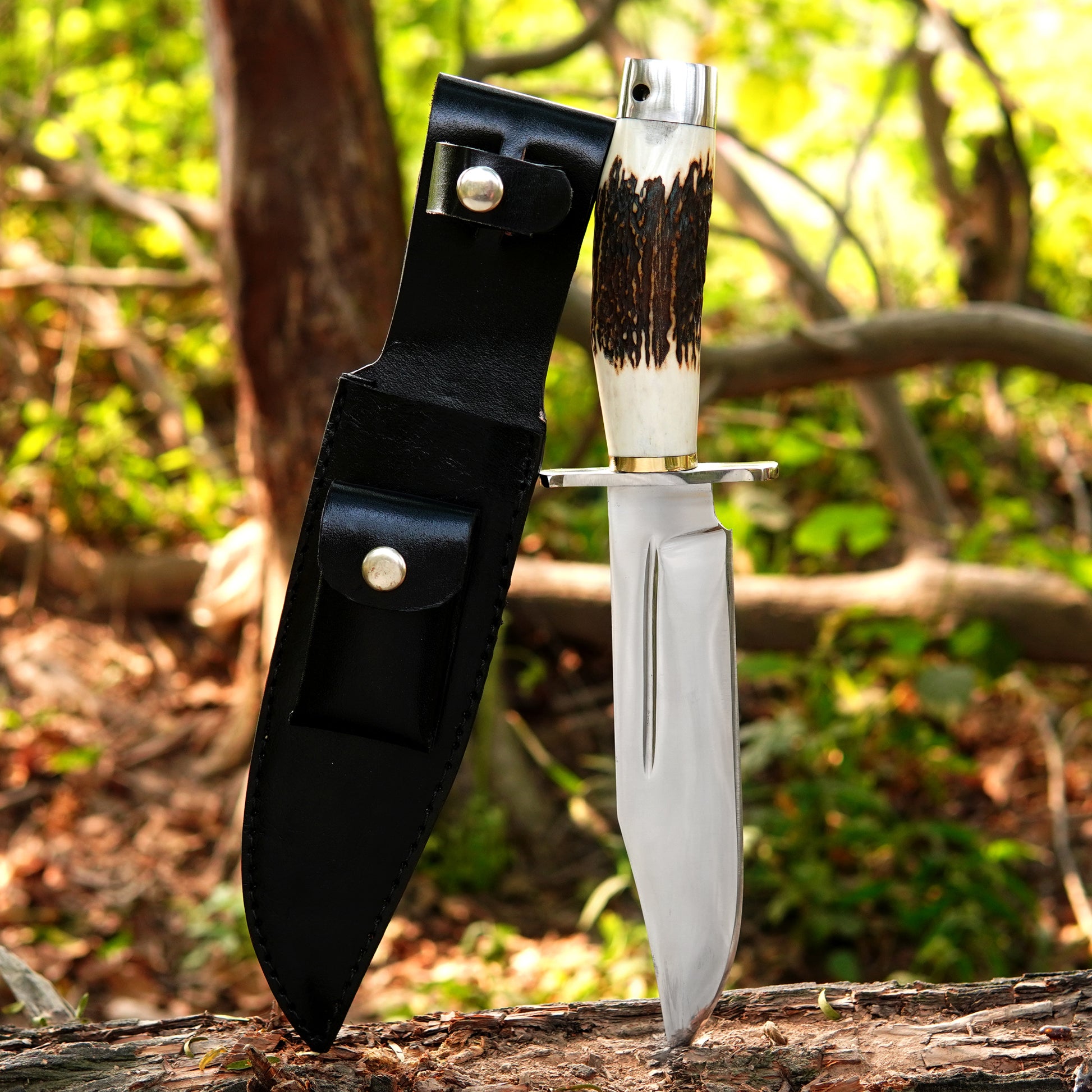 Handmade bowie style knife with polished carbon steel blade and black leather sheath outdoors.