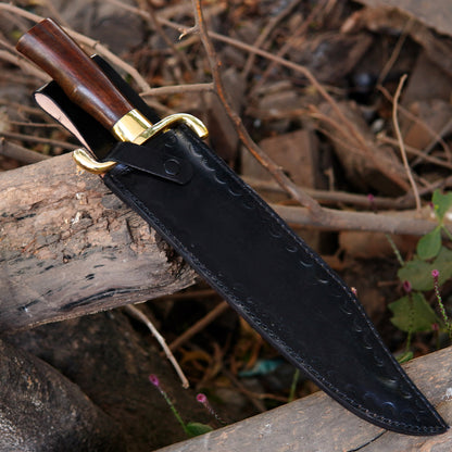Handmade bowie knife inserted in a pure leather sheath placed on wooden logs in outdoor environment. The image shows protective sheath quality, stitching detail, and safe storage design while presenting the knife as a practical outdoor tool and gift option for people who appreciate handcrafted equipment.