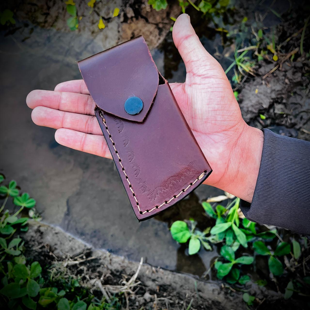 Patriotic Damascus steel pocket knife displayed with leather pouch showing handcrafted outdoor tool style.