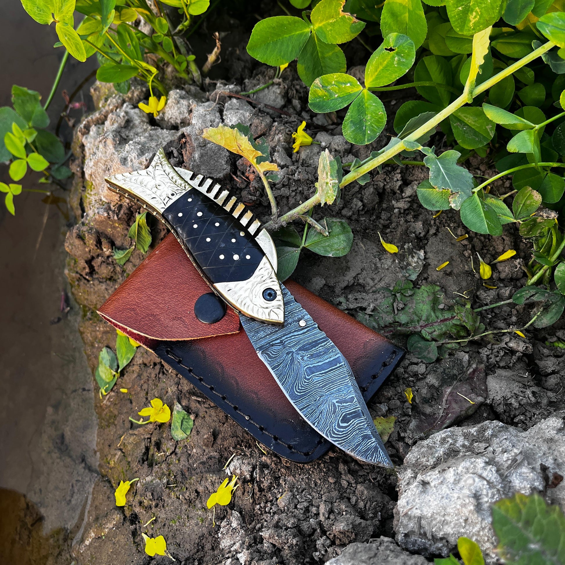 Damascus fish pocket knife with black patterned handle shown partially open displaying detailed layered steel blade pattern.