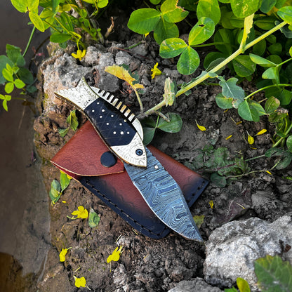 Damascus fish pocket knife with black patterned handle shown partially open displaying detailed layered steel blade pattern.