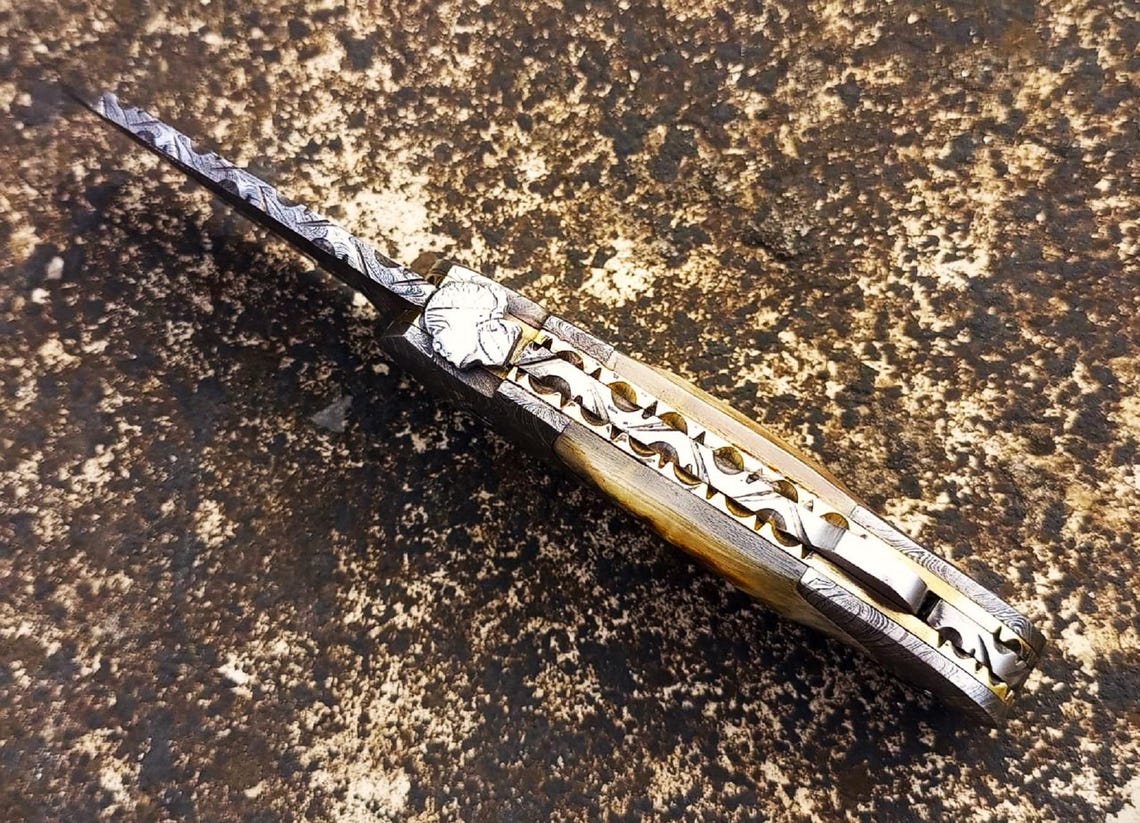 Damascus folding knife with natural ram horn handle and Damascus bolster craftsmanship.