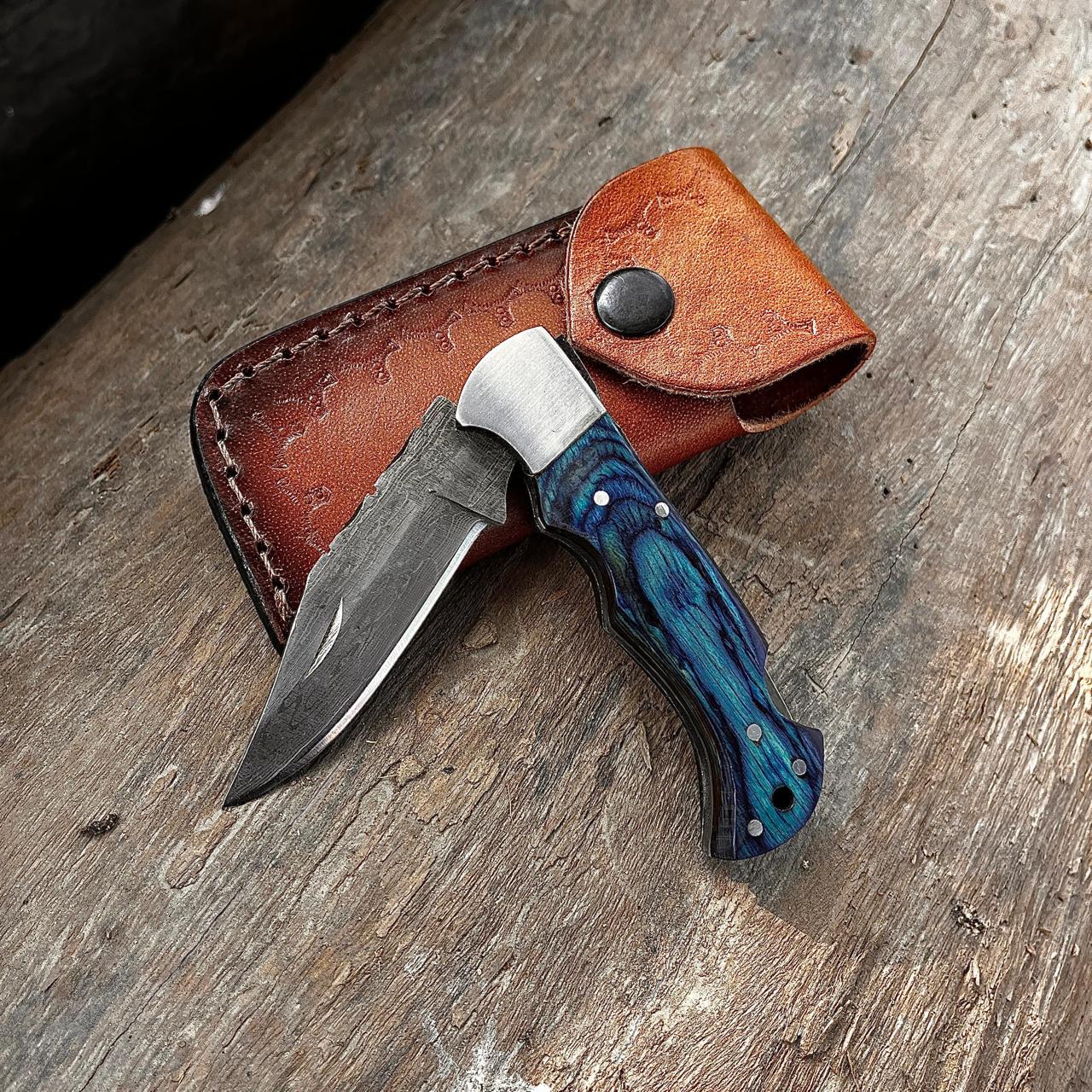 Handmade Damascus pocket knife displayed in natural outdoor setting showing knife design.