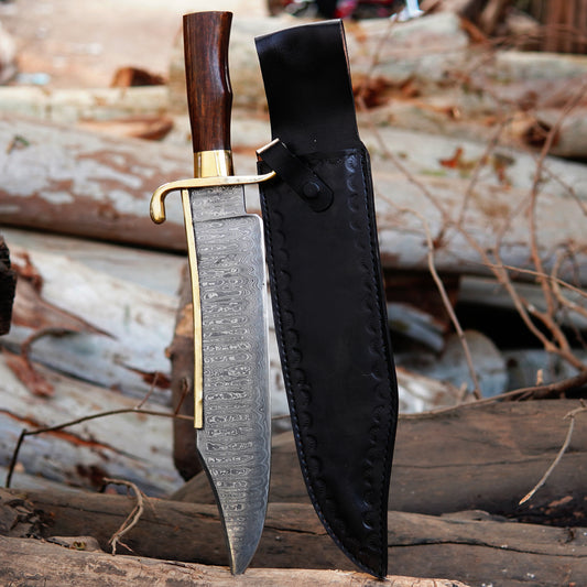 Handmade Damascus steel bowie knife placed on natural wood surface showing detailed layered blade pattern with polished wooden handle and brass guard. The image highlights craftsmanship, blade texture, and traditional outdoor knife design suitable for collectors, camping enthusiasts, and handmade knife buyers searching for premium quality fixed blade knives.
