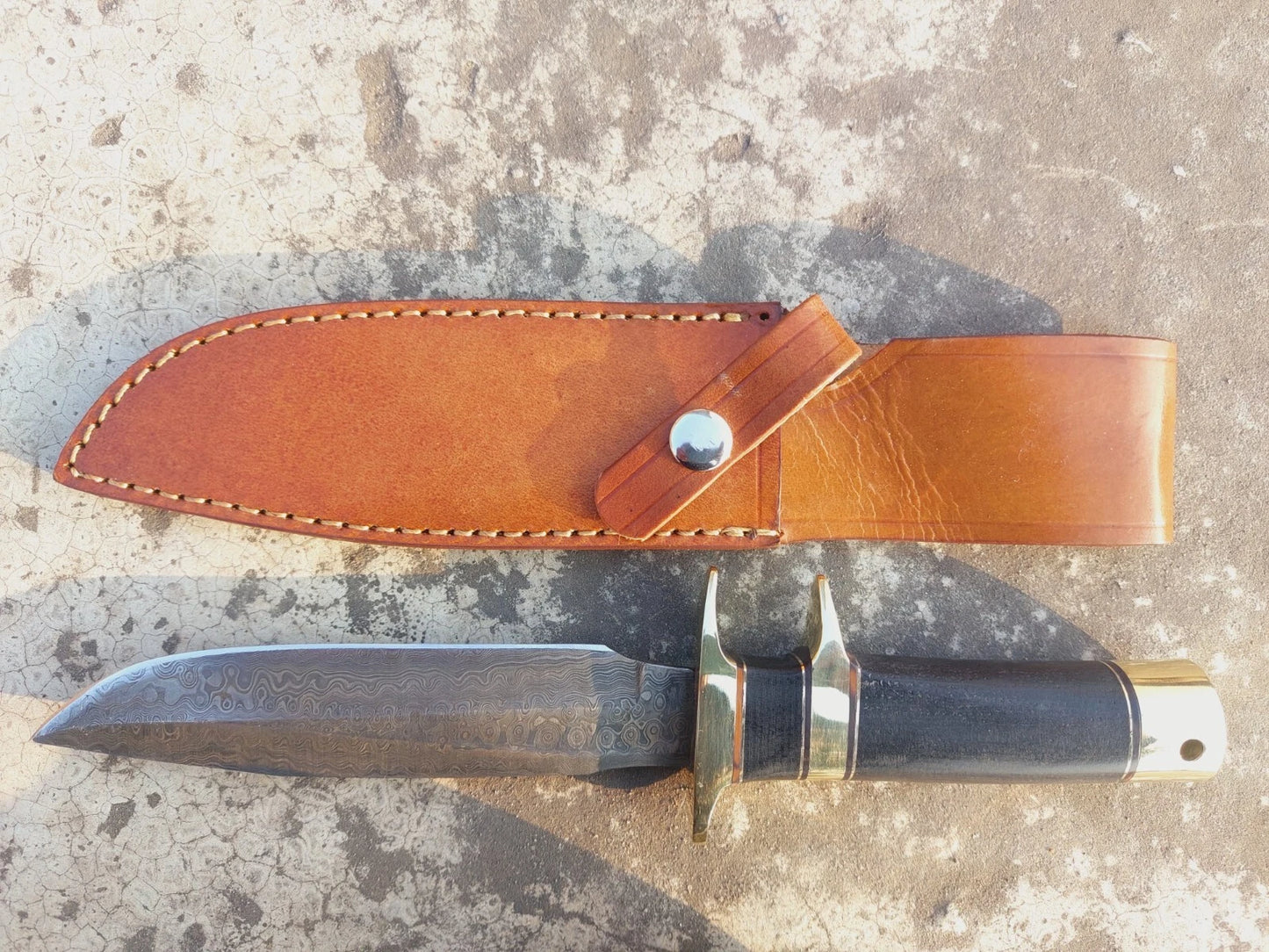 Custom handmade hunting knife crafted from Damascus steel with unique forging patterns. It features a micarta handle with brass guard and pommel, ensuring strength and balance. Includes hand-stitched leather sheath for secure outdoor carrying.