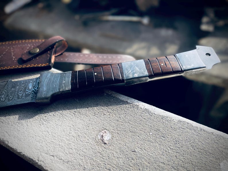 Full tang handmade Viking sword with leather sheath displayed on stone ledge.
