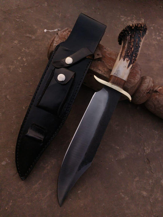 Handmade Bowie knife with mirror-dark polished carbon steel blade and black leather sheath on wooden block.