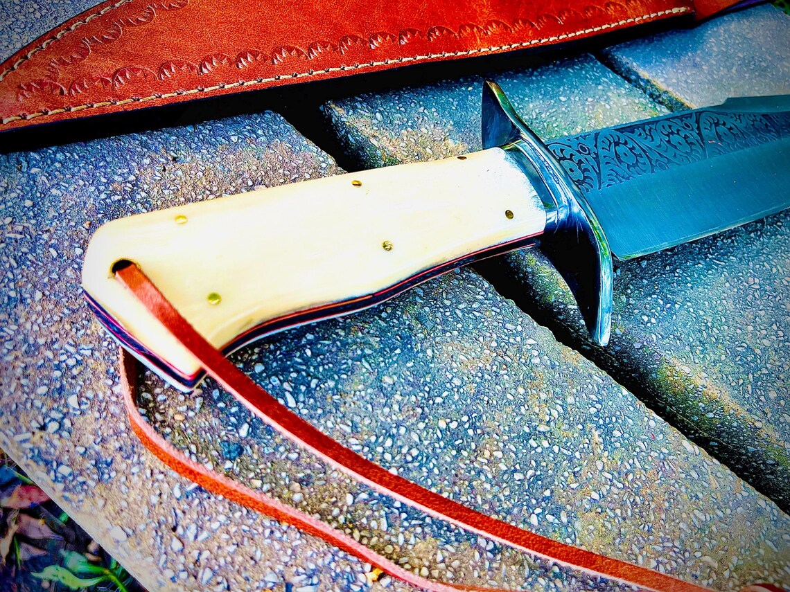 Close-up view of sandbar bowie knife handle showing polished natural material grip and engraved steel blade detail.