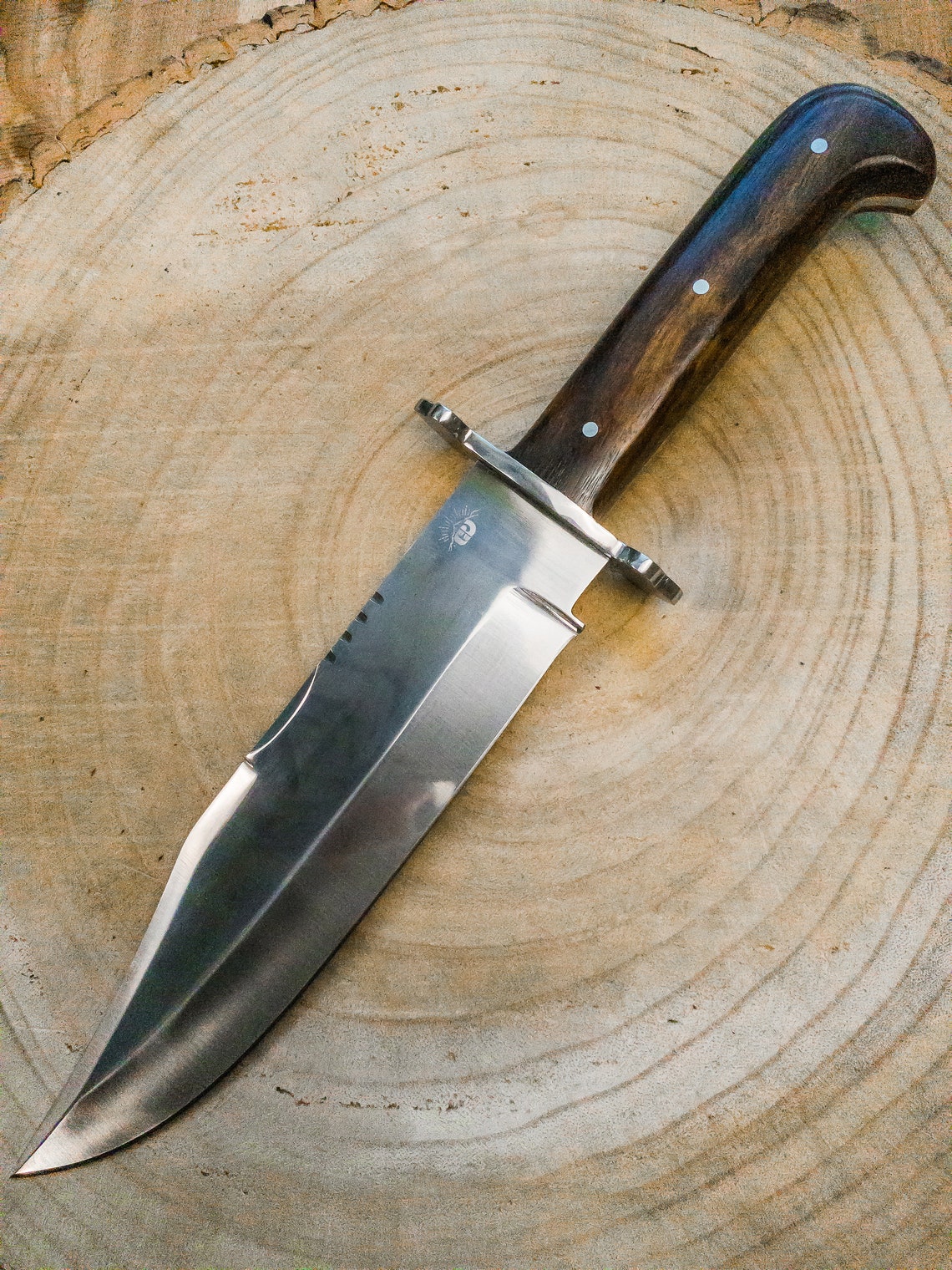 Outdoor survival Bowie knife displayed with a hand-stitched leather sheath, featuring a full tang carbon steel blade and wood handle for stability and control. Built for heavy-duty field use and long-lasting sharpness.