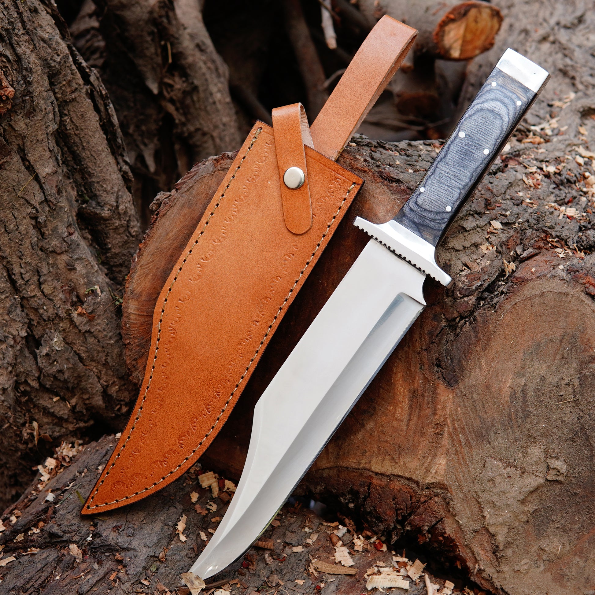Handmade bowie knife with polished high carbon steel blade placed on natural wood background showing full tang construction and strong outdoor design. The knife features a comfortable handle shape designed for secure grip and control, making it suitable for camping, bushcraft, and outdoor tasks while maintaining a clean handcrafted appearance ideal for collectors and gift buyers looking for a durable fixed blade knife.