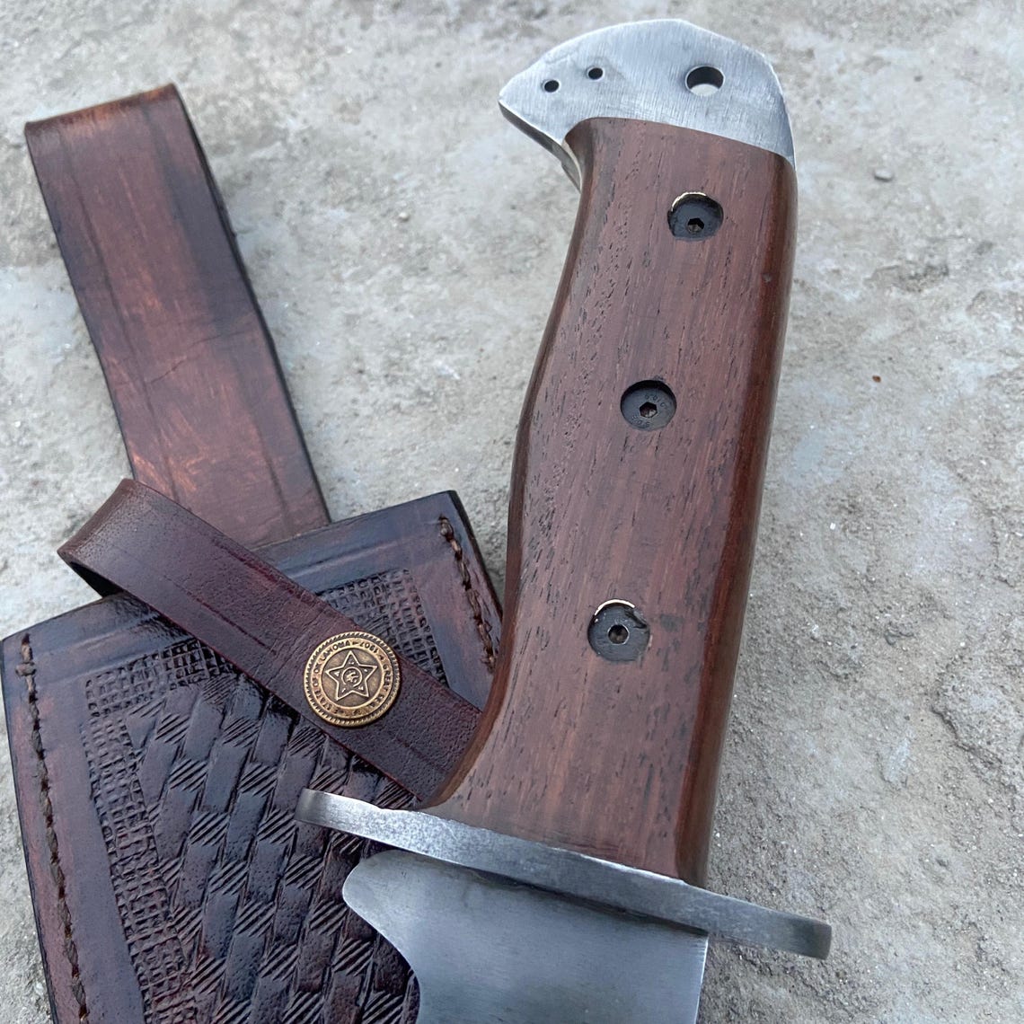 Close-up of handmade Bowie knife with full tang design and solid wood handle, showing detailed craftsmanship and brass hardware.