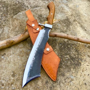 Handmade machete showing polished edge, leather sheath, and wood handle craftsmanship.